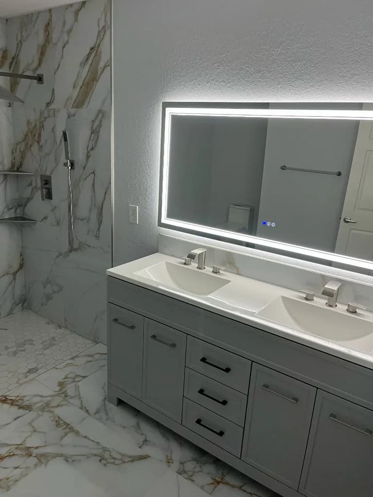 Finished bathroom with a double vanity, backlit mirror and glass shower