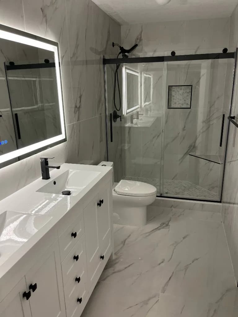 Completed bathroom with a white vanity, backlit mirror and glass shower